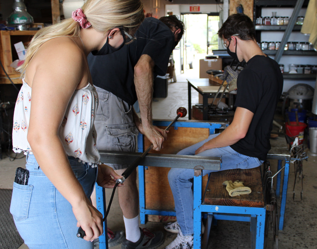 Multiple people work together to spin glass on a metal pole