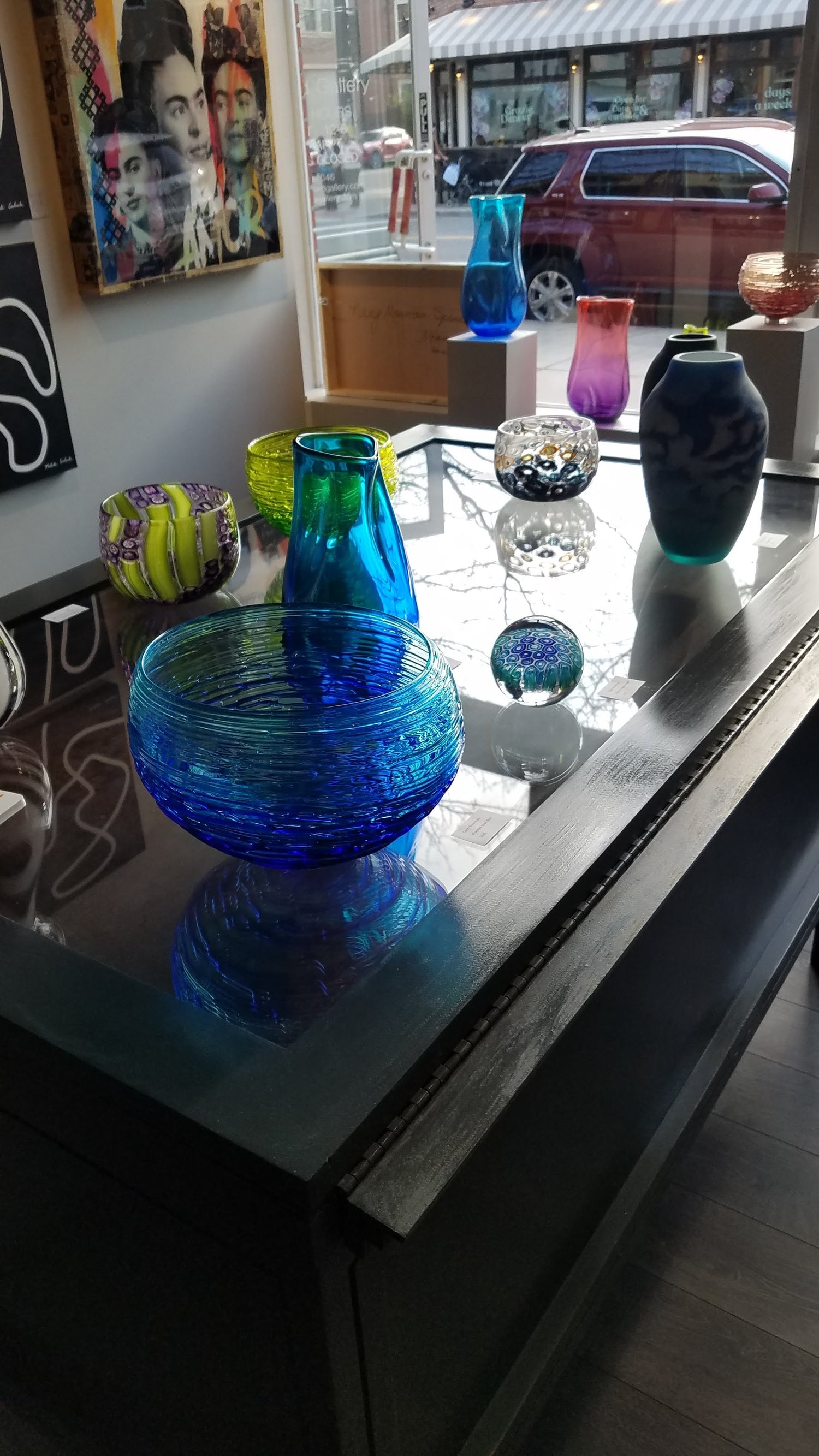 Colorful glass vases sit on a glass top table