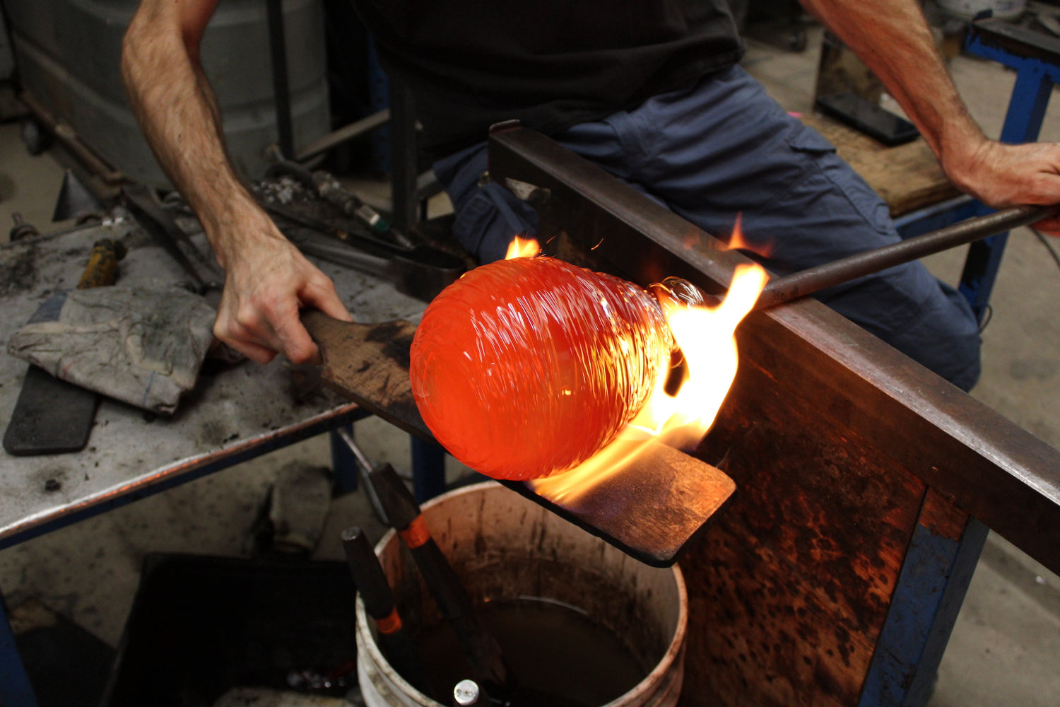A spherical glass blown object is shaped and has flames exploding off of it