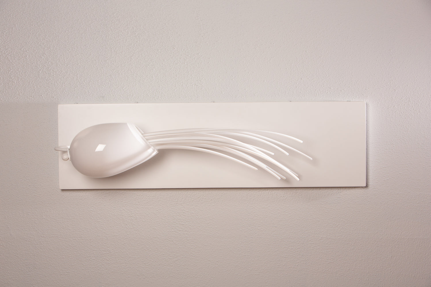 A white glass sculpture with tendrils hangs on a white wall